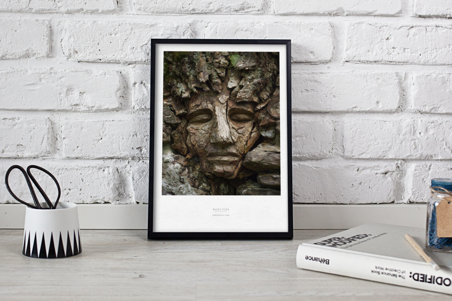 Framed artwork of a stone face on a white brick wall background