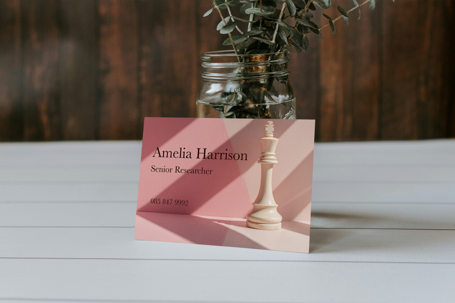 Business card with a pink gradient background featuring a chess piece and vase with greenery on a wooden surface.