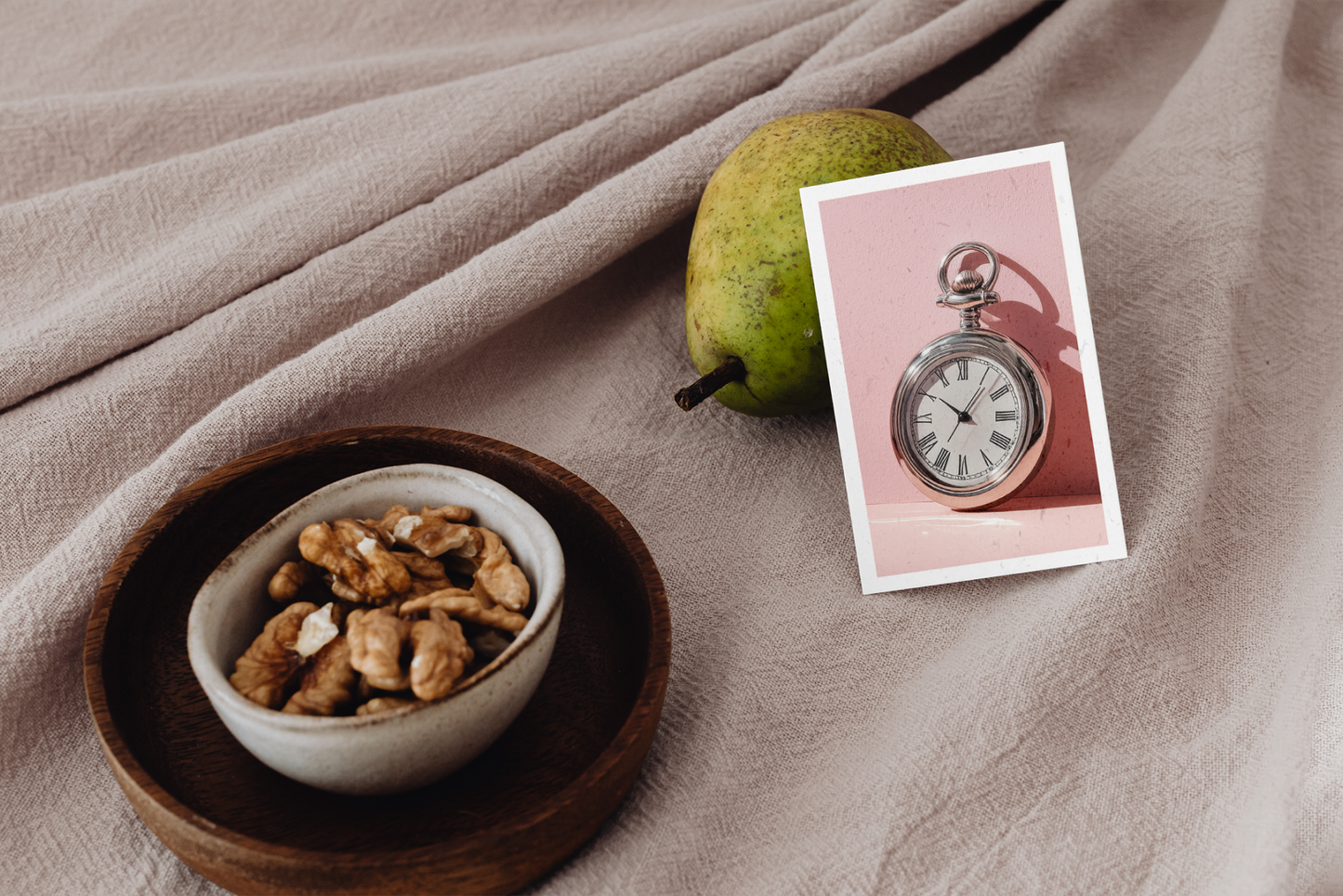 Bowl of nuts, pear, and pocket watch card on a textured surface
