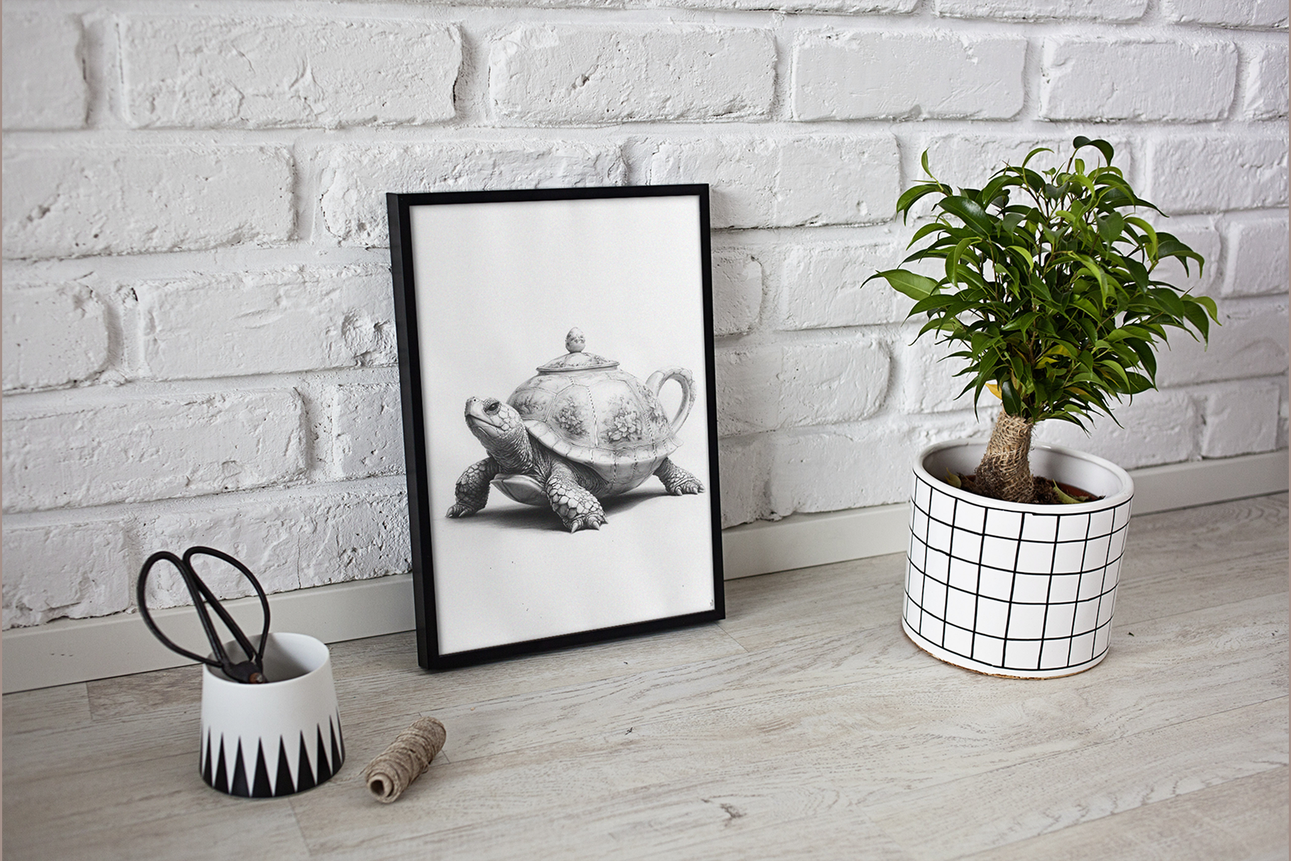 Framed black and white artwork of a teapot on a brick wall background, with a potted plant and decorative items.