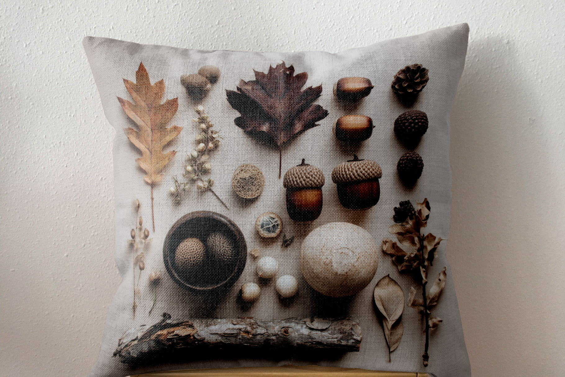 Decorative pillow with natural elements like leaves, acorns, and twigs on a neutral background