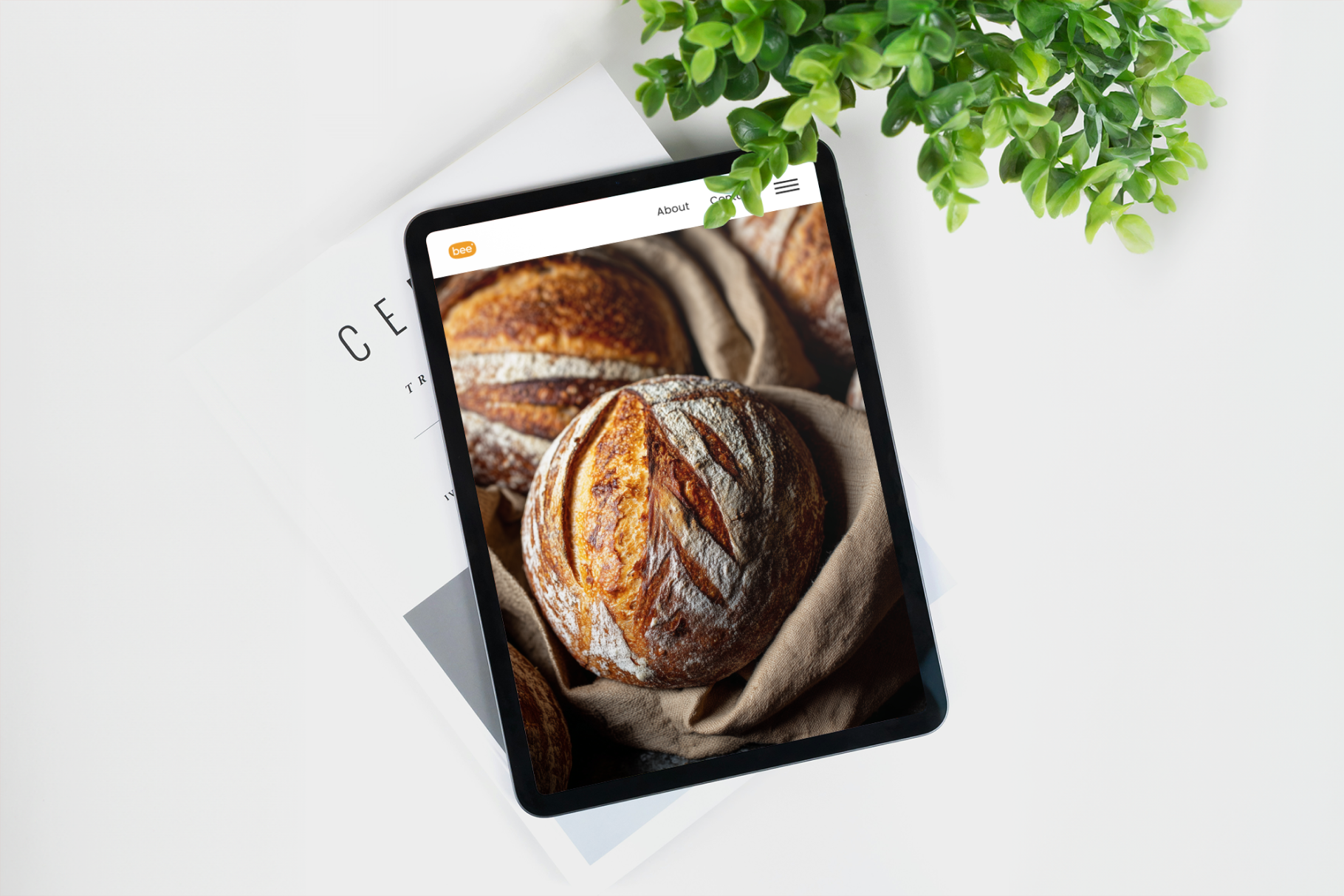 Tablet displaying bread images on a white surface with a plant