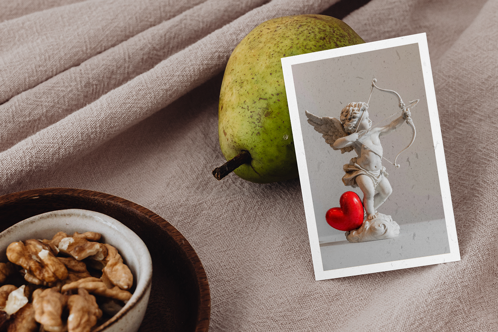 Pear, bowl of nuts, and photo of Cupid with a heart on a beige fabric background