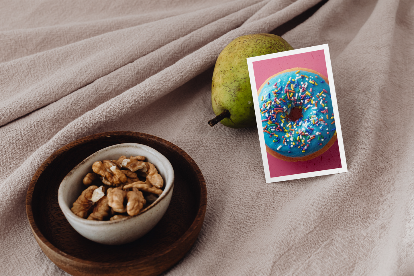Bowl of nuts, pear, and card with donut on beige fabric