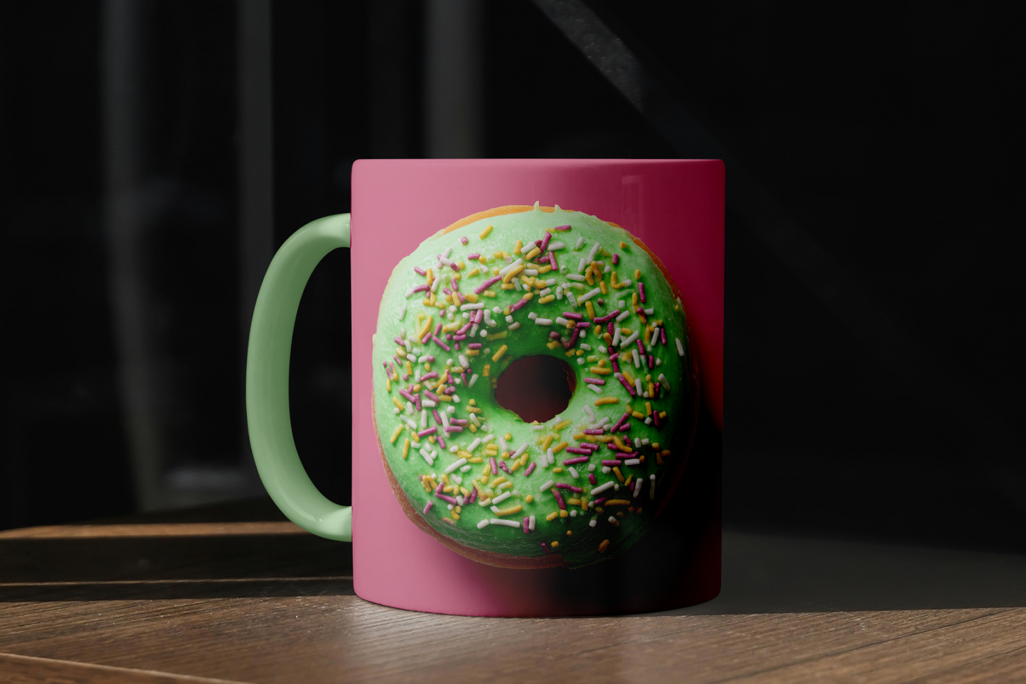Pink mug with a green donut design featuring sprinkles on a dark background