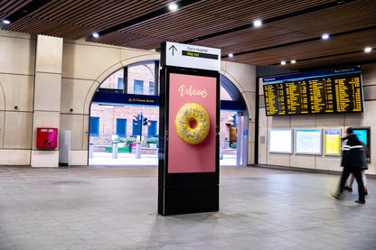 Digital display board with a donut advertisement in a train station.