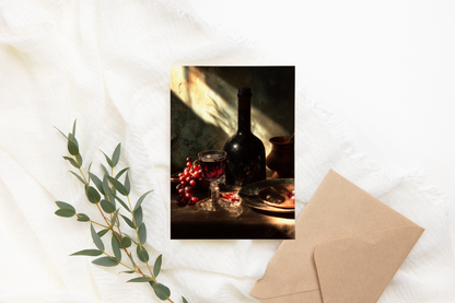 Framed artwork of a bottle and glass on a textured surface with a card and eucalyptus branch.