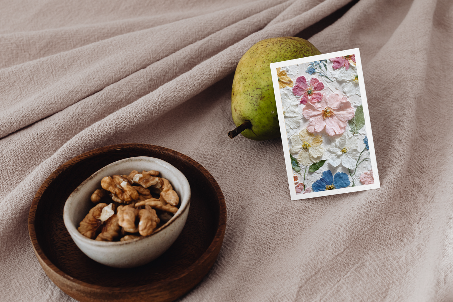 Bowl of nuts, pear, and floral card on a textured surface