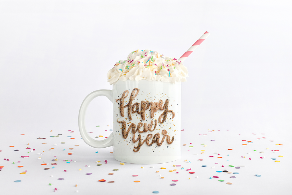 Mug with 'Happy New Year' text, whipped cream, and a straw on a white background with confetti.