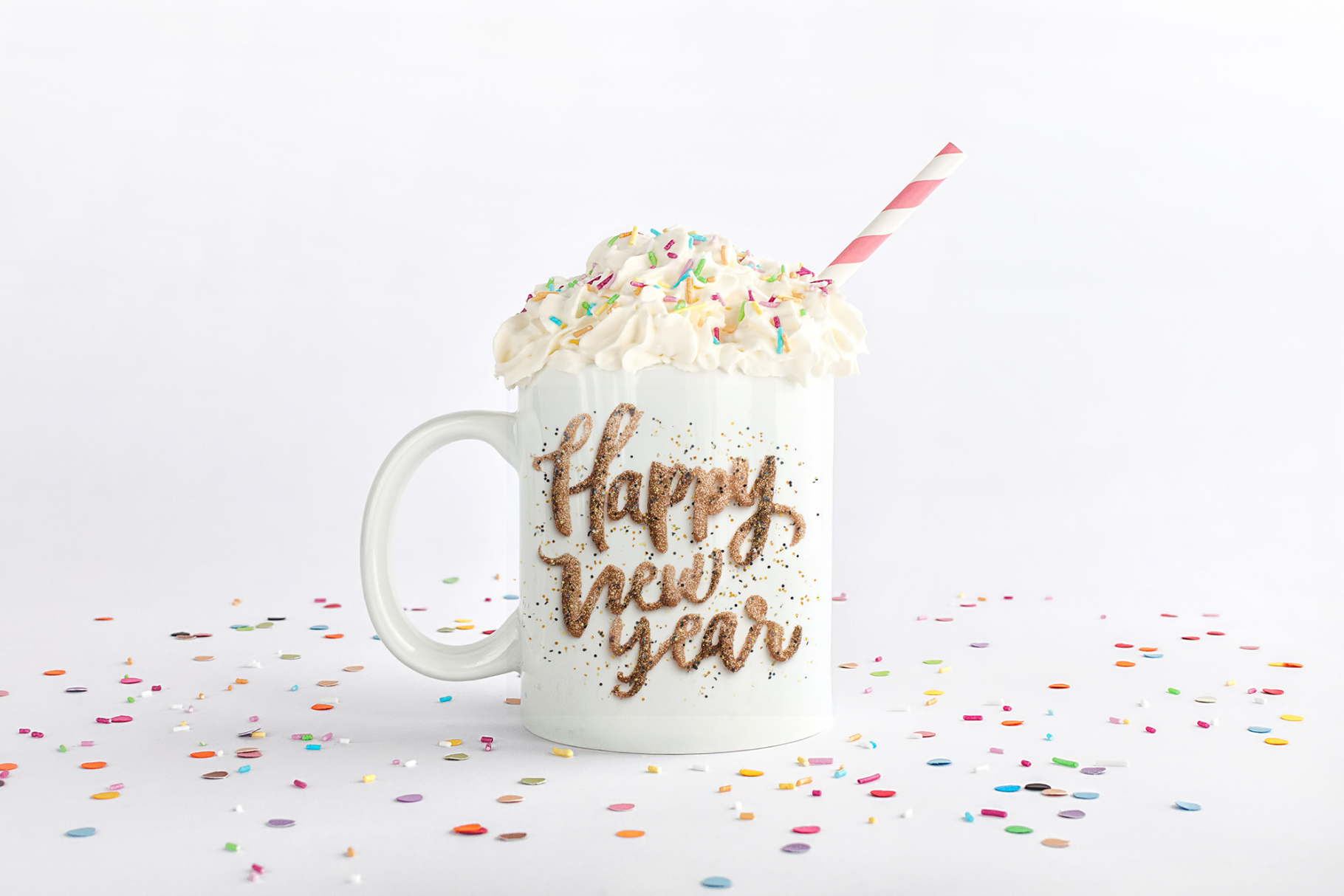 Mug with 'Happy New Year' text, whipped cream, and a straw on a white background with confetti.