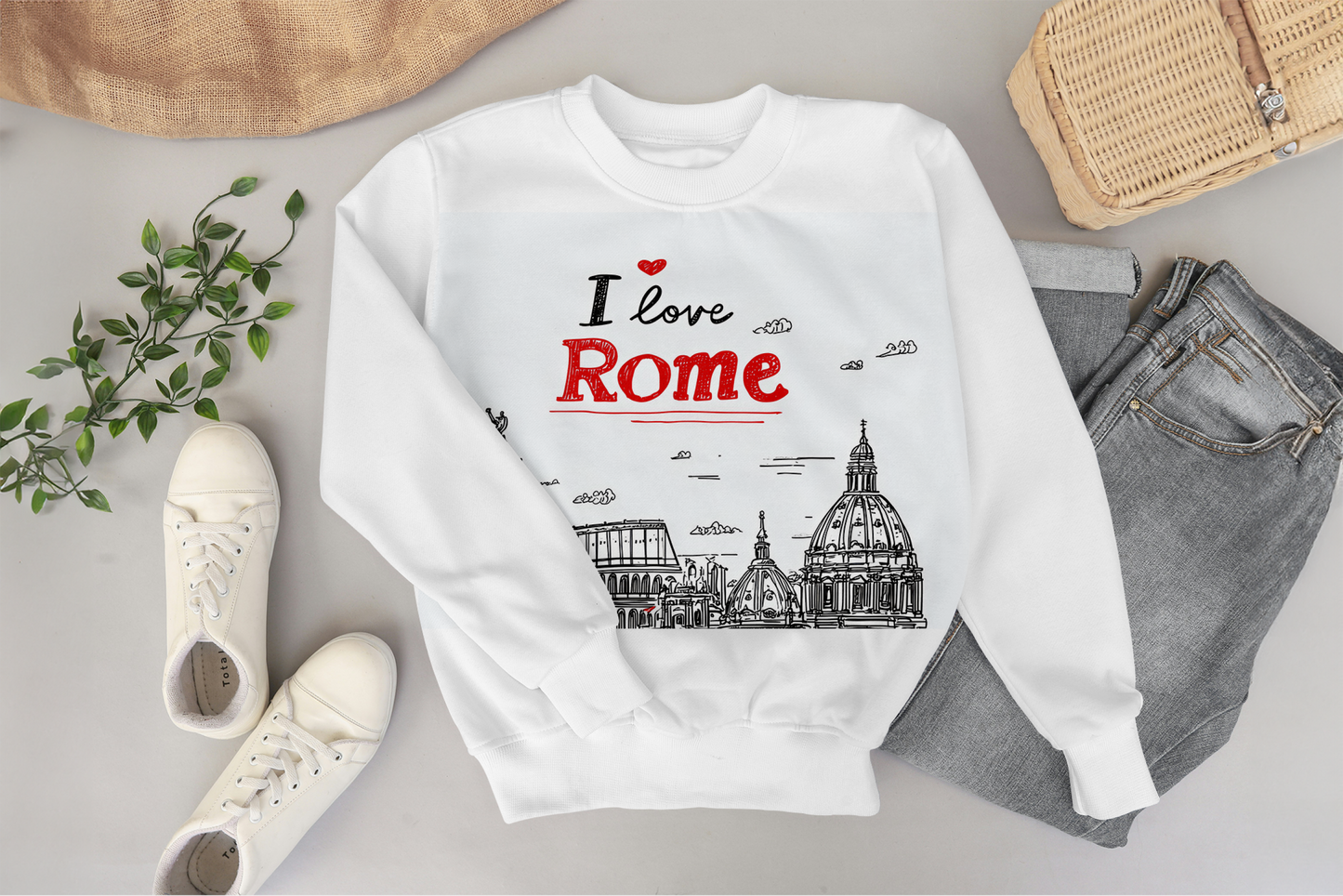 White sweatshirt with 'I love Rome' design on a gray surface with shoes and jeans.