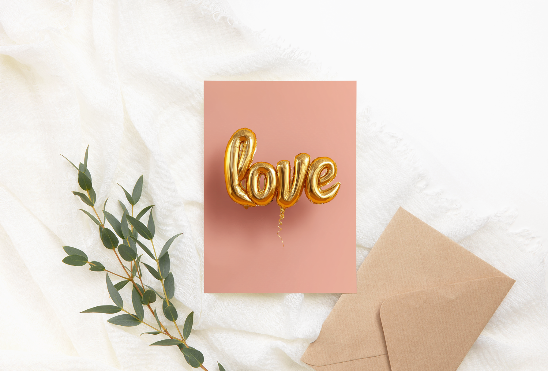 Card with 'love' balloons on a pink background, accompanied by a brown envelope and green leaves.