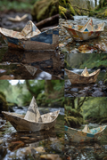 A collage of five photographs showing small paper boats made from folded newspaper floating on shallow water in a forest stream. The boats have a weathered tan, blue, and brown printed newspaper pattern.