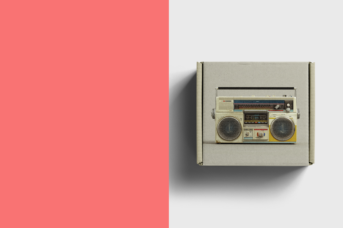 A vintage-style boombox radio mounted on a light gray wall, with a large solid coral-pink color block occupying the left side of the frame.