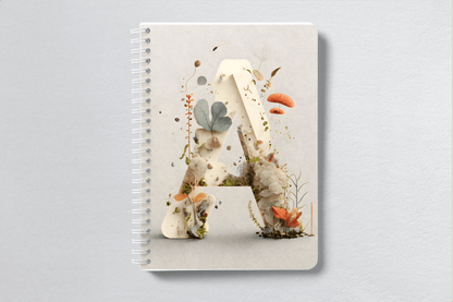 A photograph of a notebook cover with the letter A made of fungal elements and forestry themed colours.